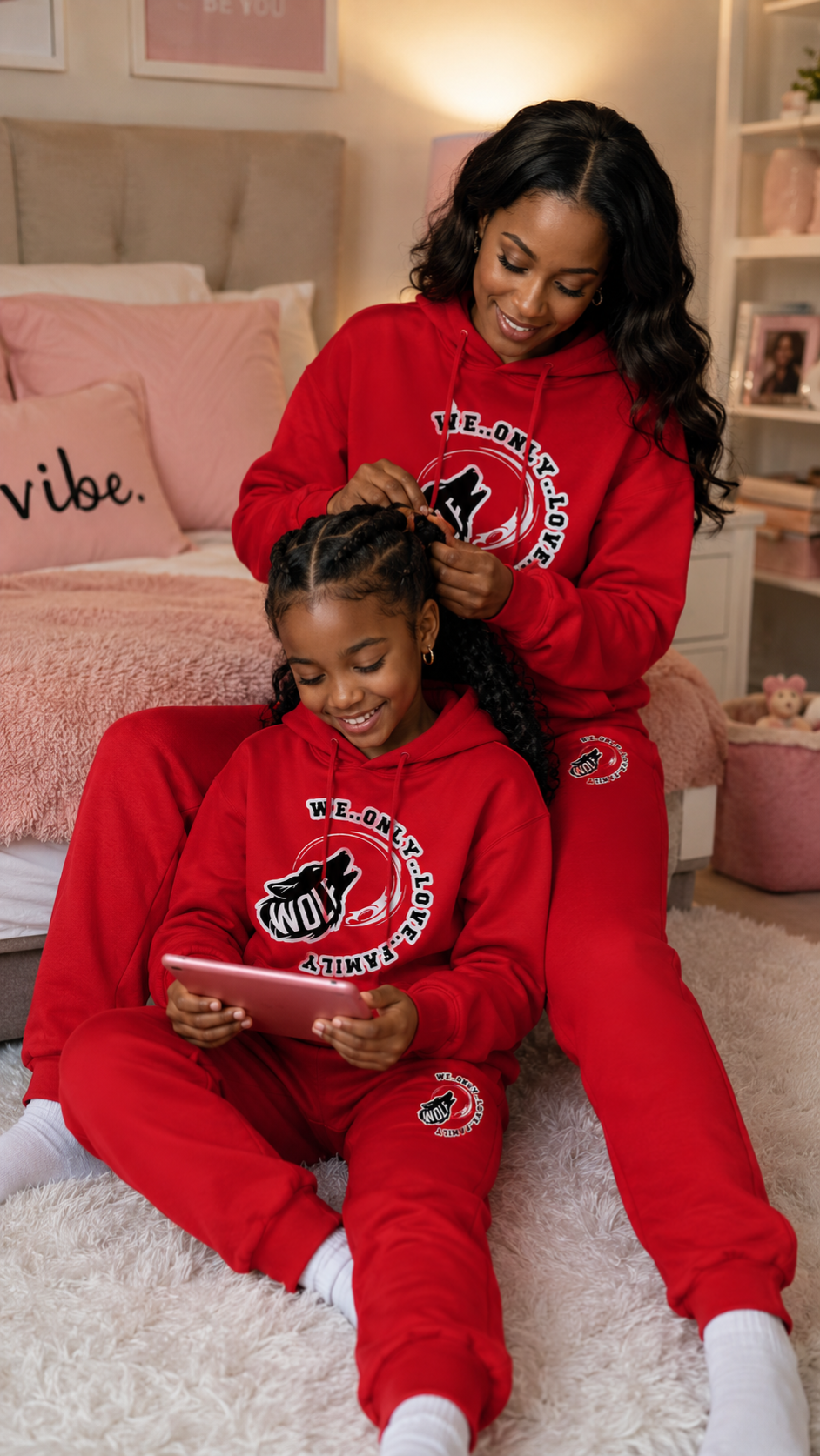 Two people, mother and daughter in matching red sweatshirt and pants sitting on a bed in a bedroom.